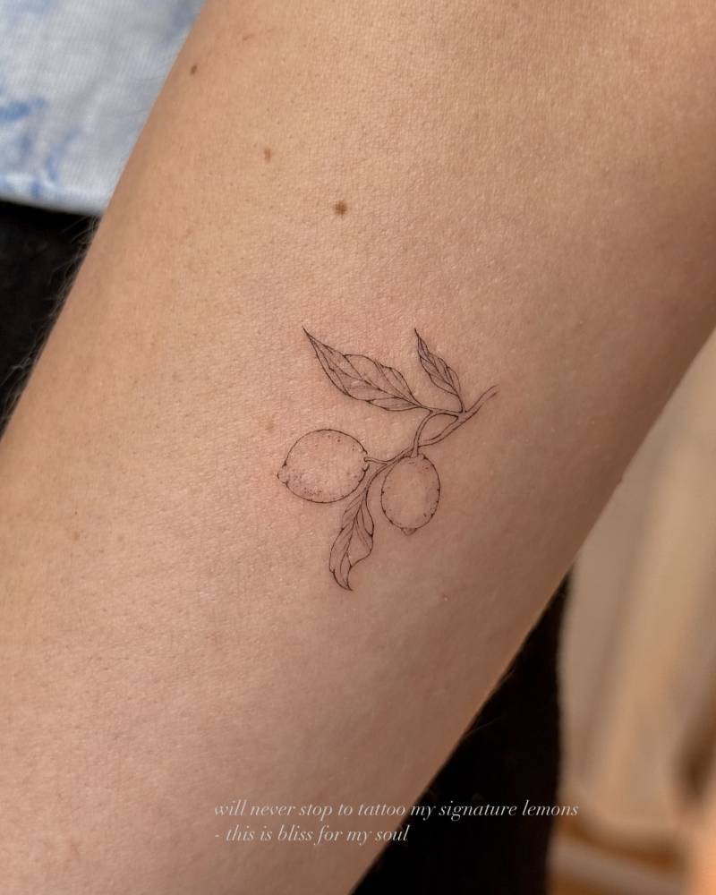 Little lemons tattooed on the inner forearm, done in fine line style.