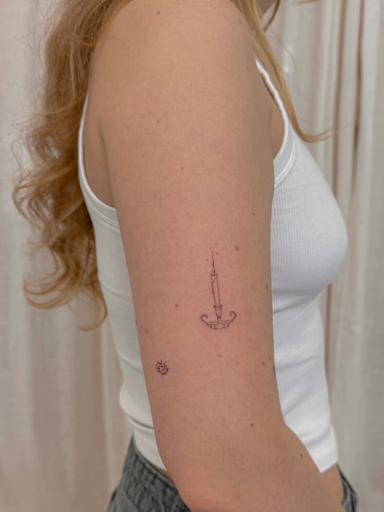 Candle tattoo in fine line style located on the upper arm.