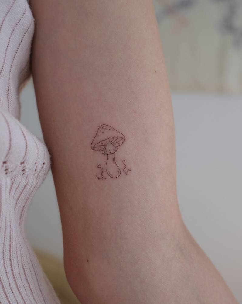 Mushroom tattoo in fine line style located on the inner arm.