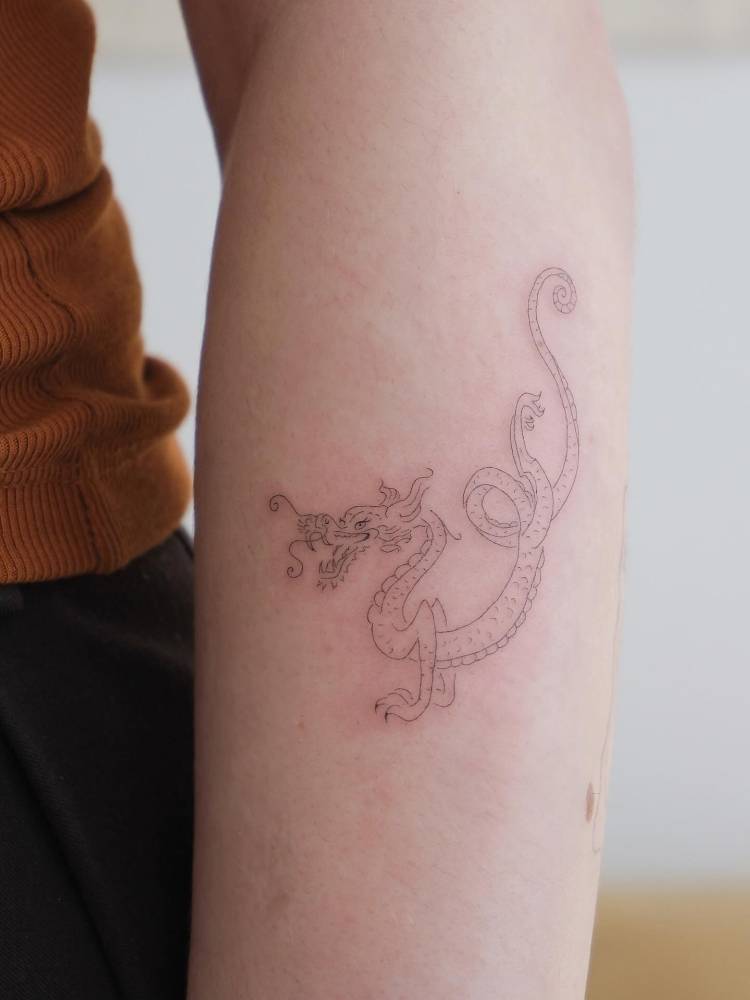 Dragon tattoo in fine line style located on the forearm.
