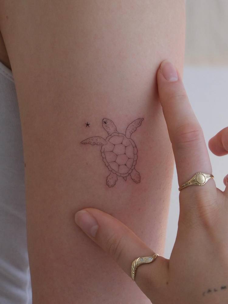 Cute fine line style turtle tattoo placed on the upper arm.