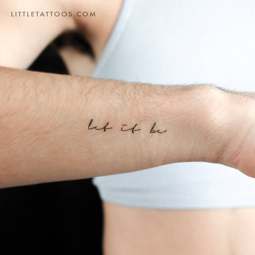 Small "let it be" temporary lettering tattoo located on the wrist.