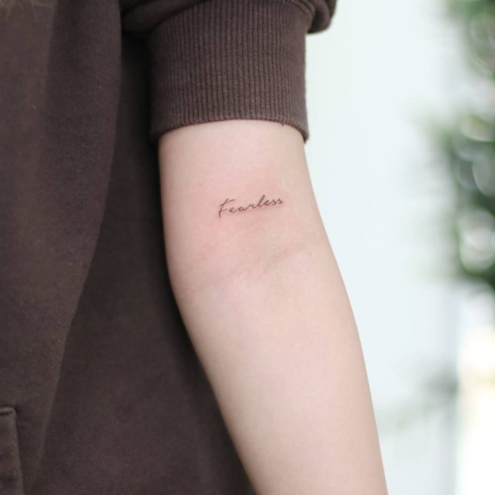 Handwritten font word "fearless" tattoo located on the bicep.