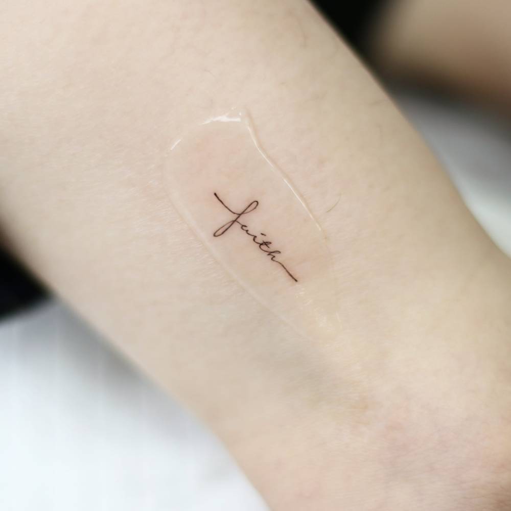 "Faith" cross lettering tattoo located on the thigh.