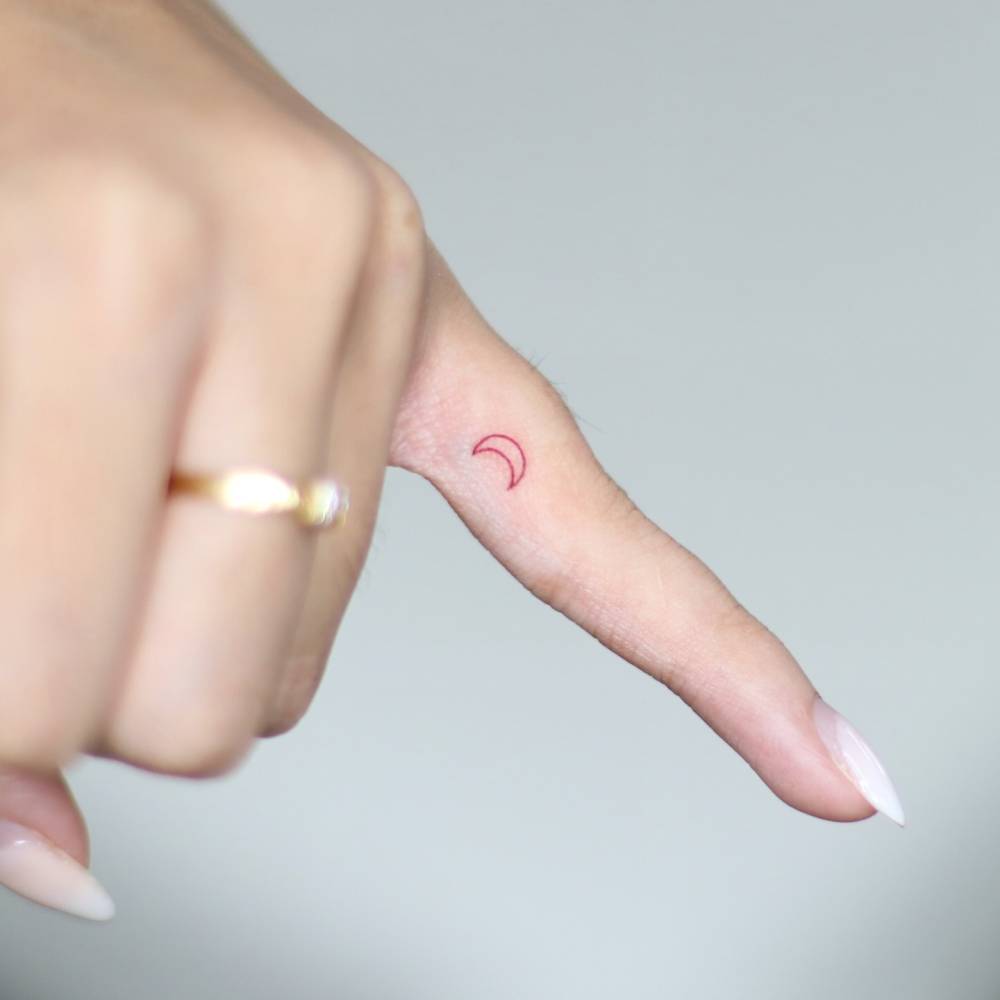Minimalistic style red crescent moon tattoo located on the finger.