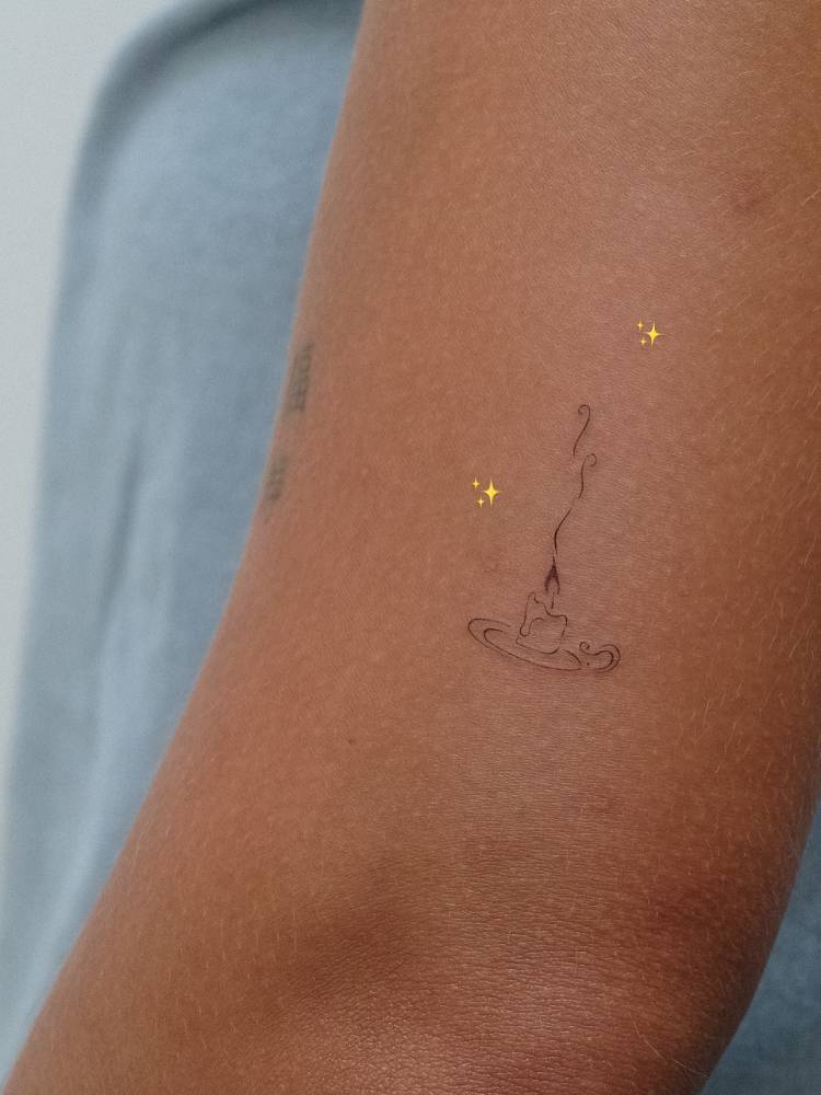 Burning candle tattoo located on the upper arm, done in fine line style.