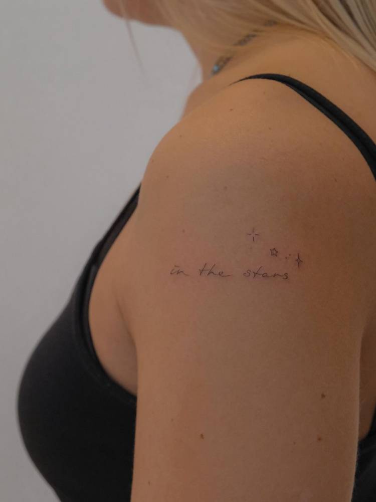 Lettering tattoo that says "in the stars" done on the upper arm.
