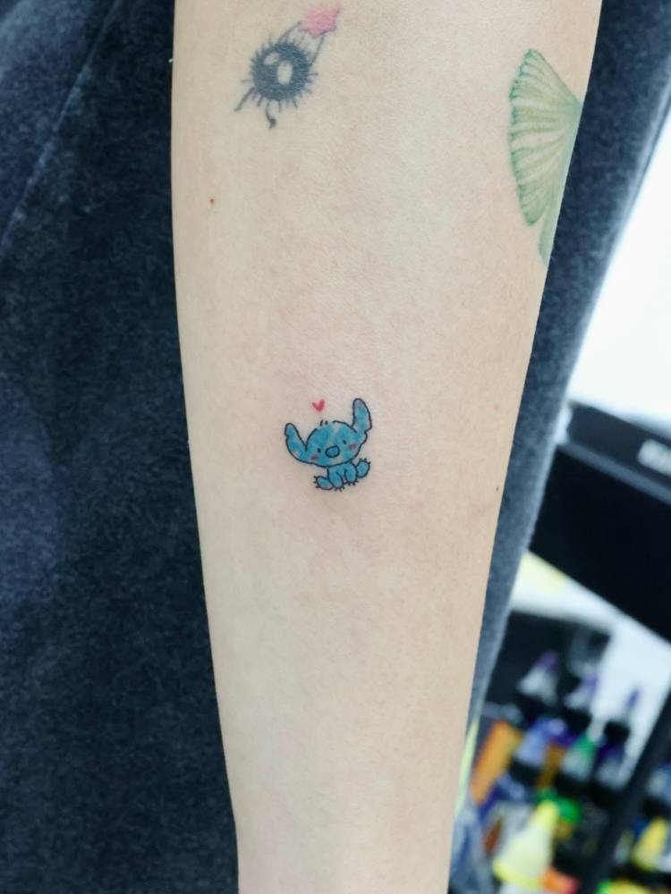Stitch tattoo located on the forearm, done in cartoon style.