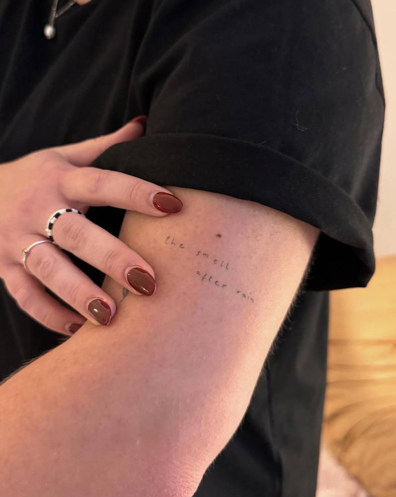 Healed "the smell after rain" lettering tattoo located on the upper arm.