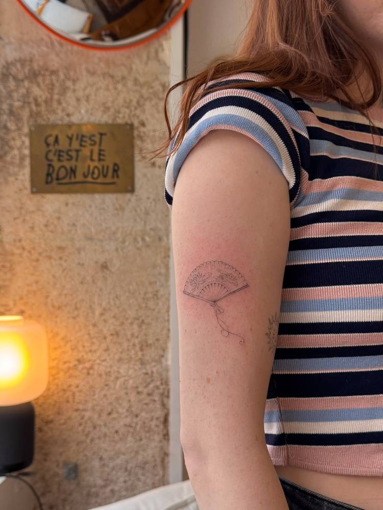 Fine line style hand fan tattoo located on the upper arm.