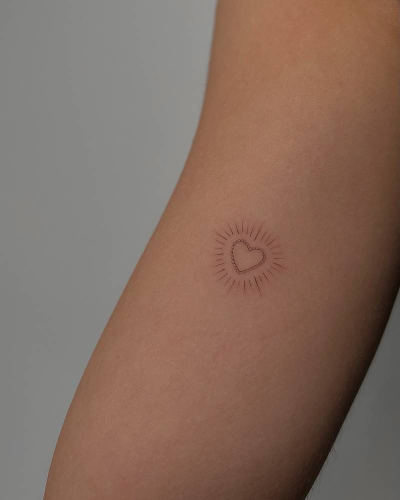 Shiny heart tattoo in fine line style located on the inner arm.