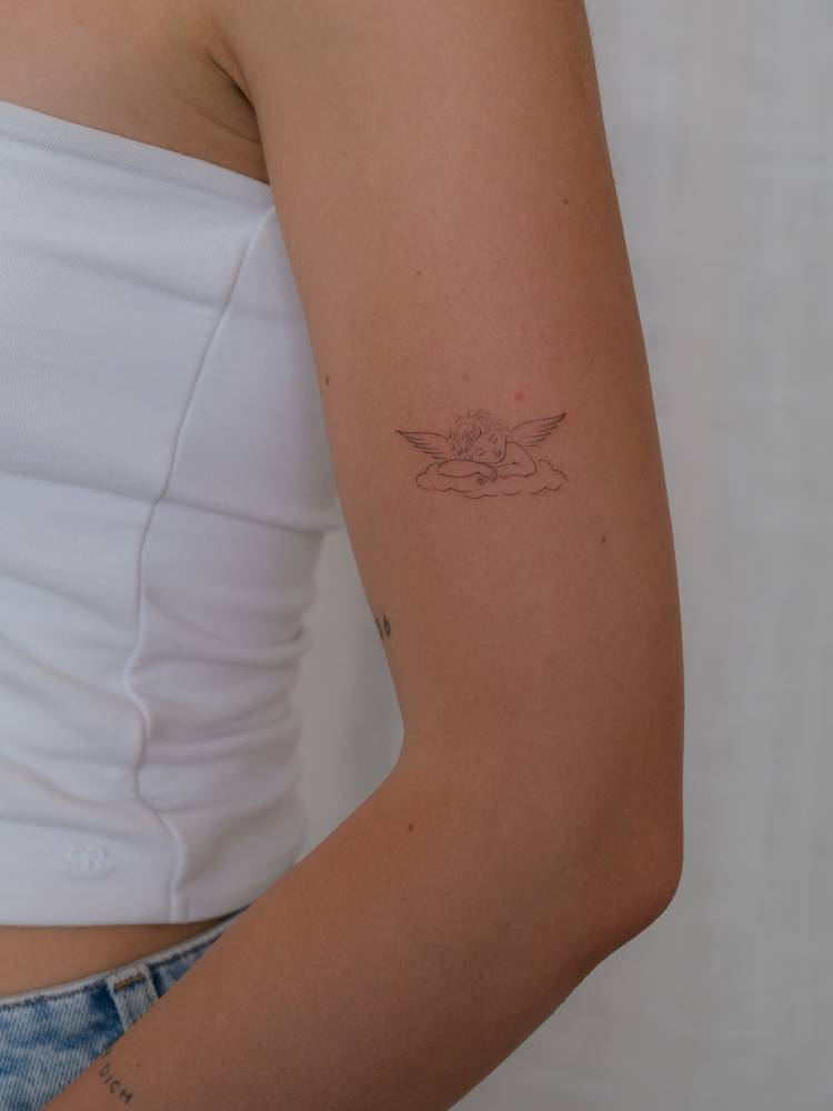 Sleeping cherub tattoo in fine line style placed on the upper arm.