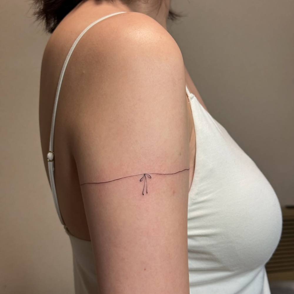 Bow bracelet tattoo located on the upper arm, fine line style.