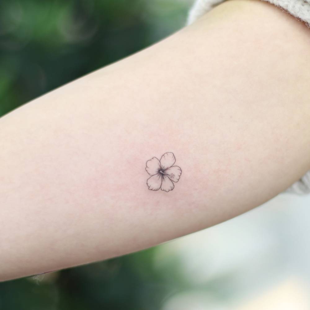 Fine line style tiny hibiscus flower tattoo located on the inner arm.