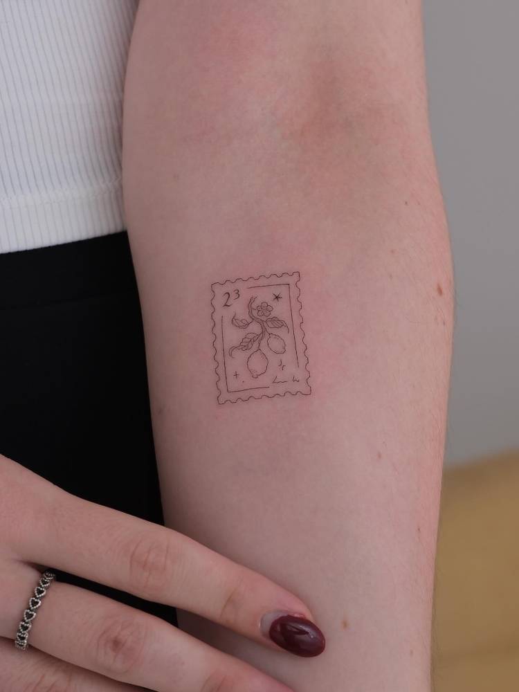 Lemon stamp tattoo in fine line style placed on the inner forearm.