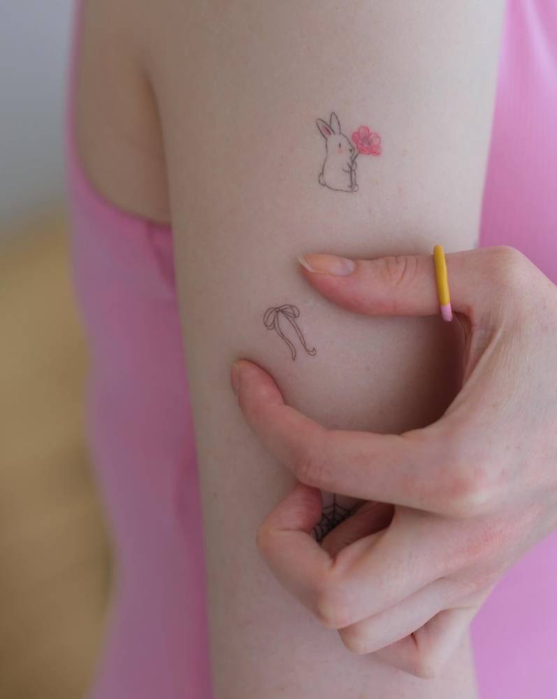 Fine line style minimalistic bow tattoo located on the upper arm.