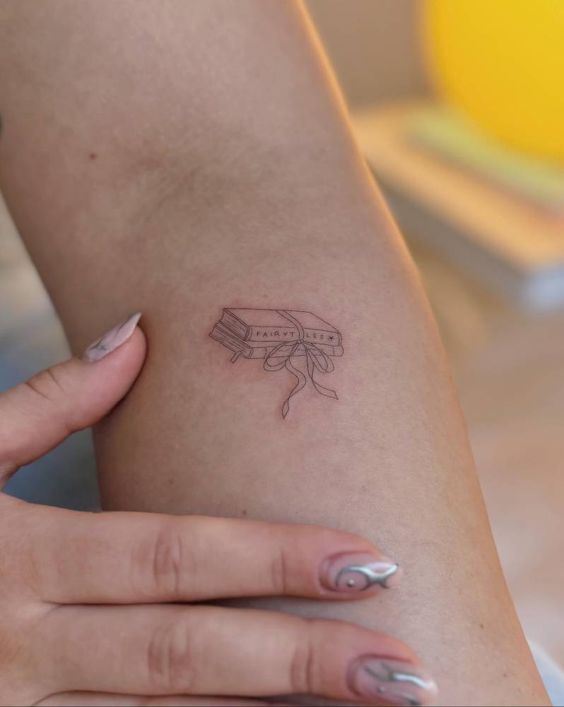 Fine line style books tattoo located on the forearm.