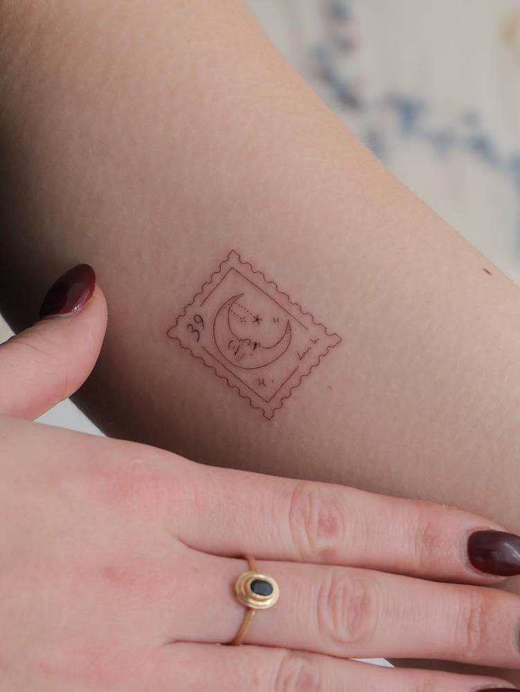 Fine line style crescent moon stamp tattoo located on the inner arm.