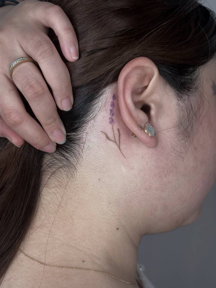 Watercolor style lavender tattoo located behind the ear.
