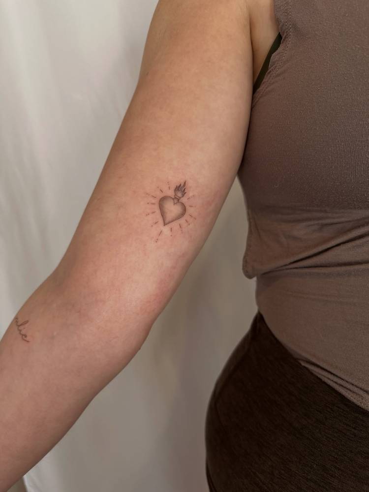 Flaming heart tattoo in illustrative style located on the inner arm.