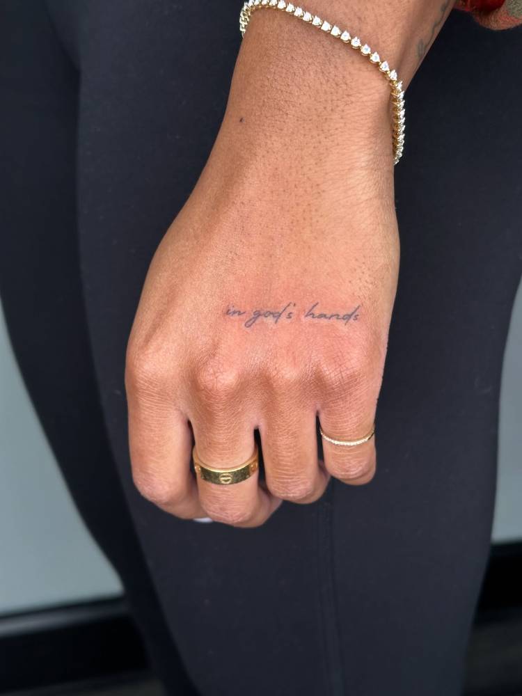 Handwritten font "in God's hands" lettering tattoo.