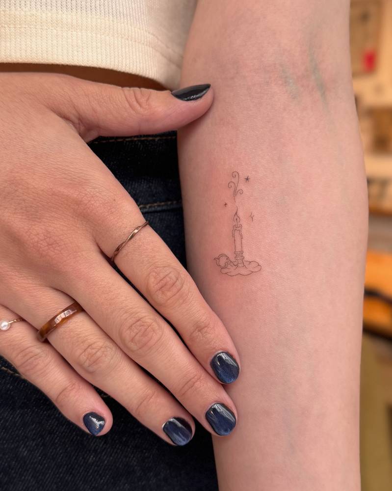 Little candle tattoo located on the inner forearm, done in fine line style.