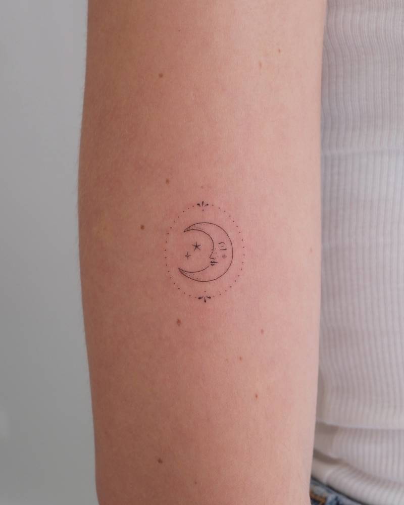 Little moon face tattoo in fine line style done on the upper arm.
