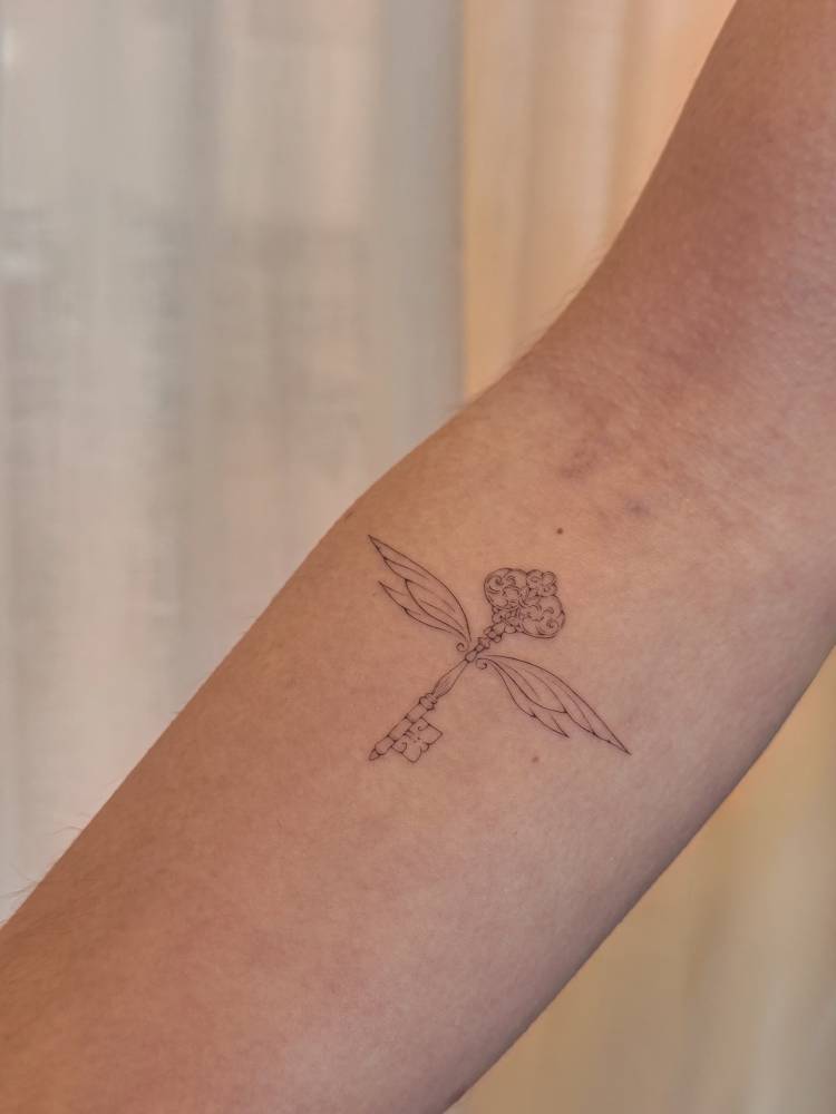 Winged keys in fine line style placed on the inner forearm.