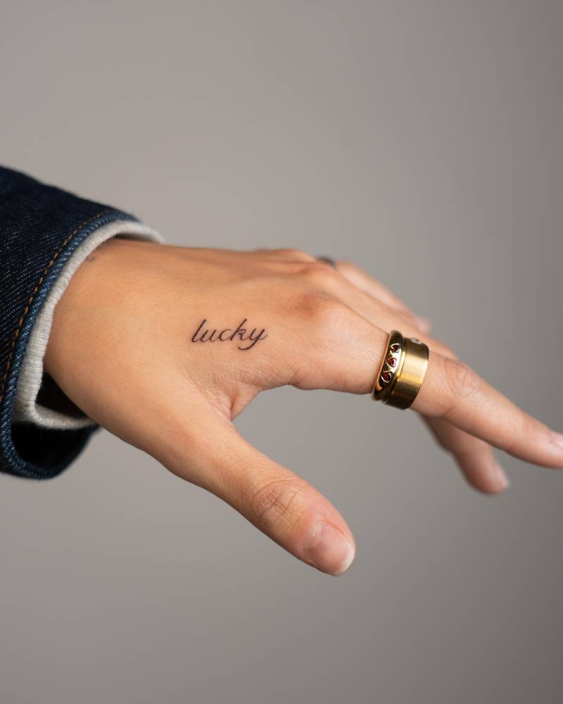 Word "lucky" in script font tattooed on the hand.