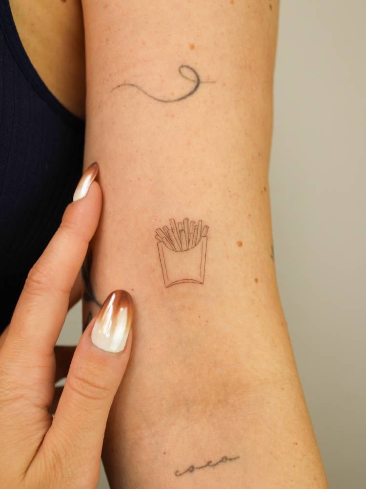 French fries tattoo in fine line style located on the bicep.