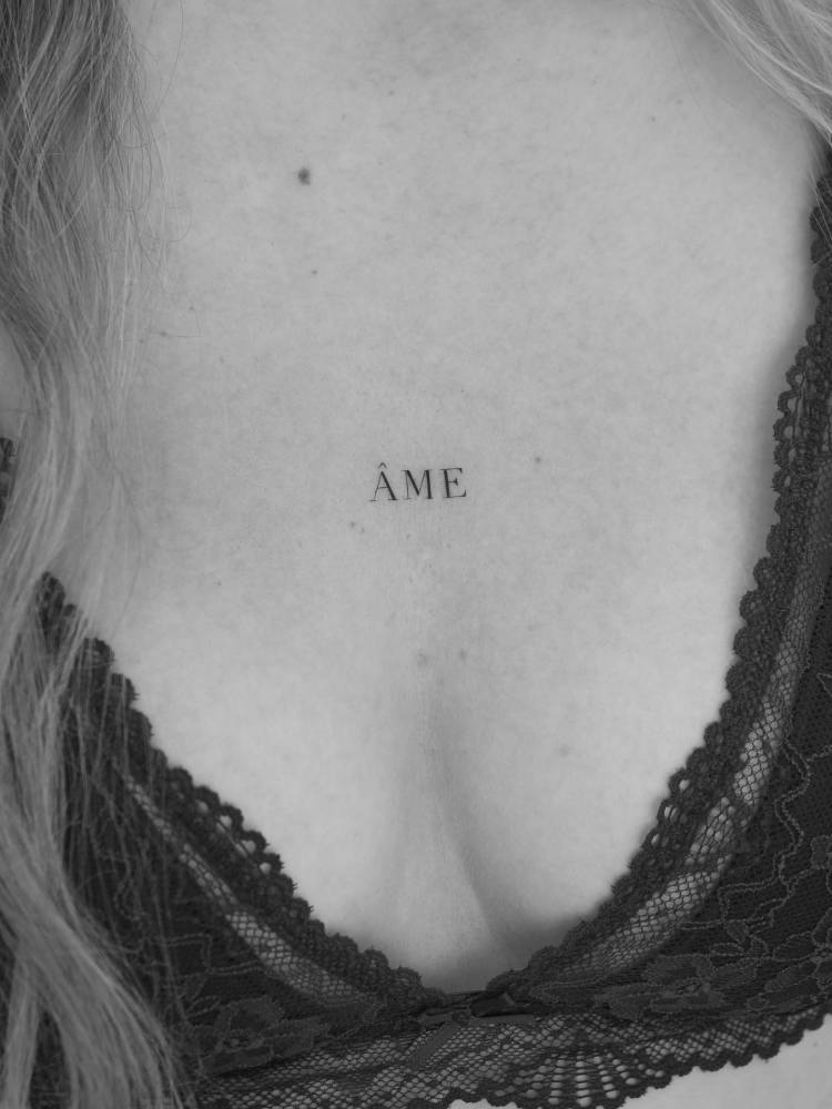 "Âme" lettering tattoo in serif font located on the sternum.
