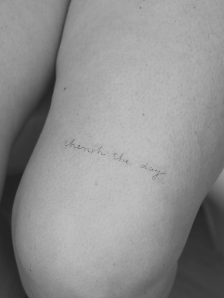 "Cherish the day" lettering tattoo placed on the thigh.