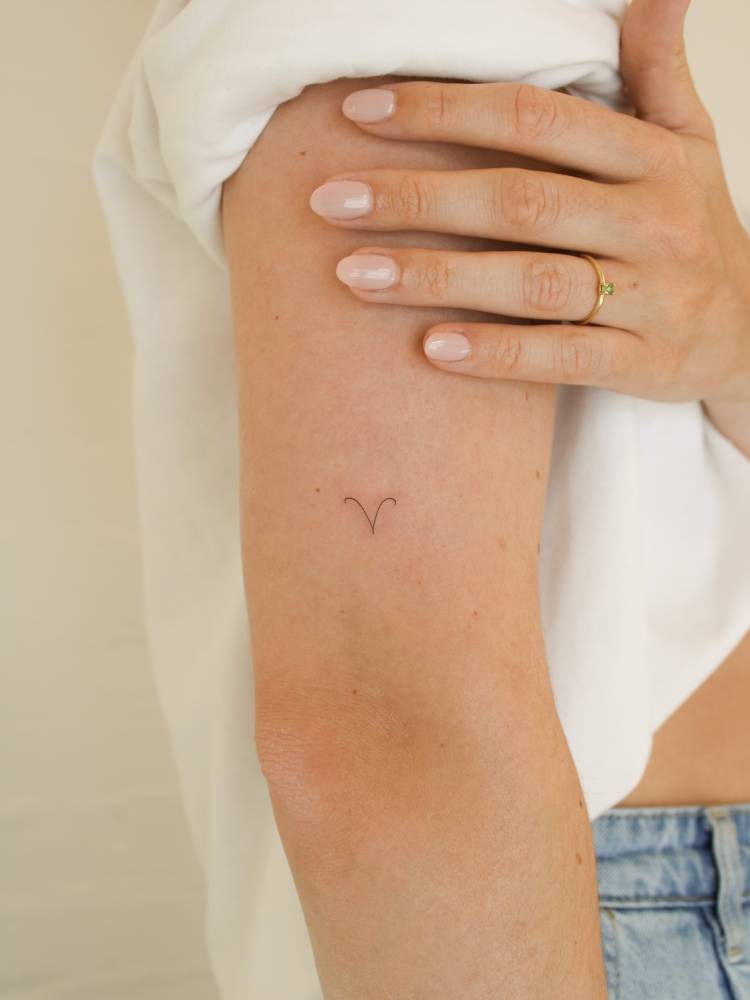 Little minimalistic Aries zodiac symbol tattooed on the upper arm.