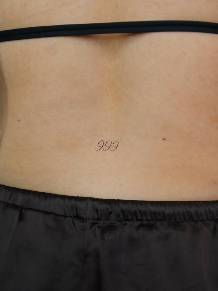Angel number "999" tattoo located on the lower back.