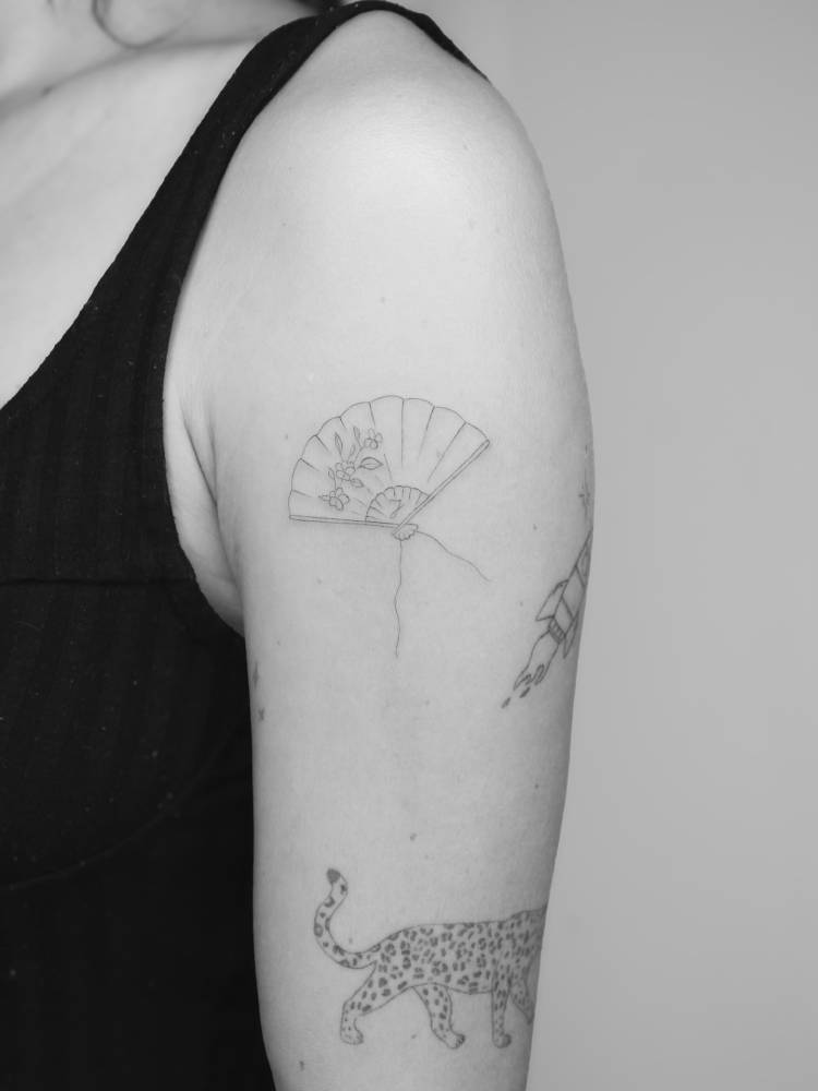 Hand fan tattoo in fine line style located on the upper arm.