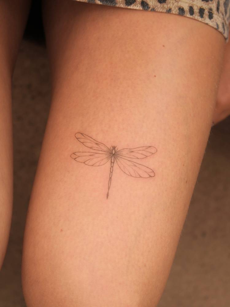Dragonfly tattoo placed on the thigh, done in fine line style.