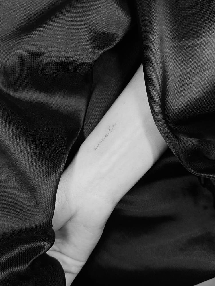 Handwritten font word "create" tattooed on the wrist.