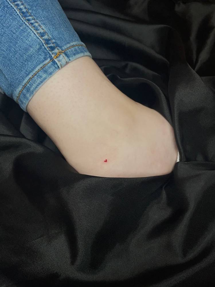 Micro red heart tattoo located on the ankle, minimalistic style.
