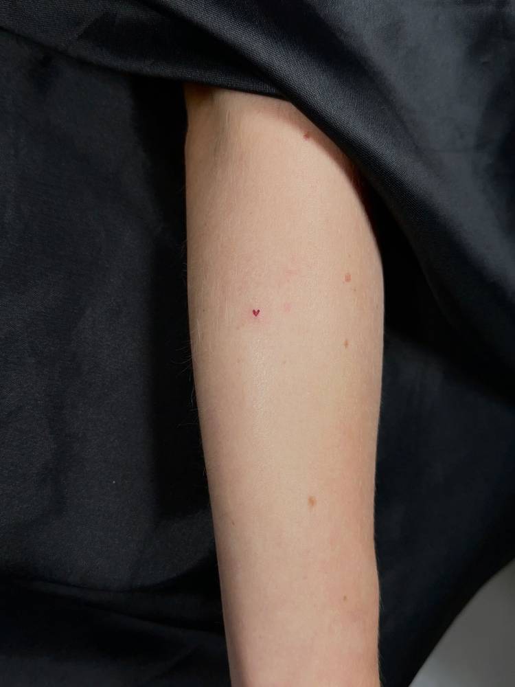 Red heart tattoo done on the forearm, minimalistic style.