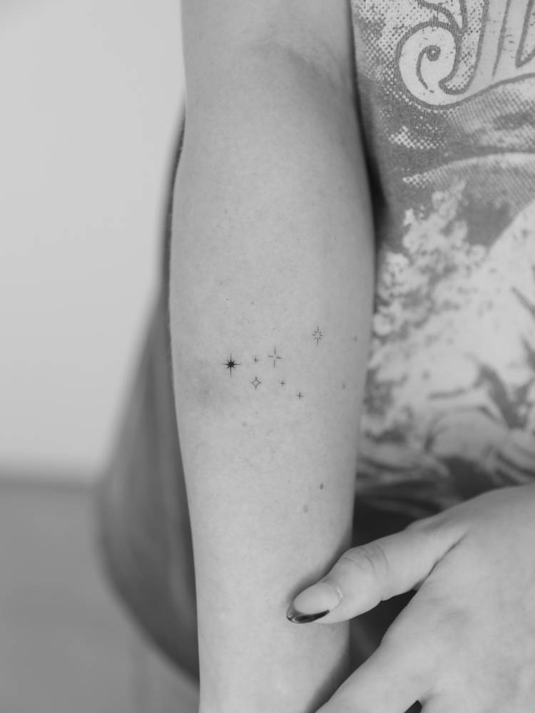 Sparkling stars tattooed on the forearm, done in minimalistic style.