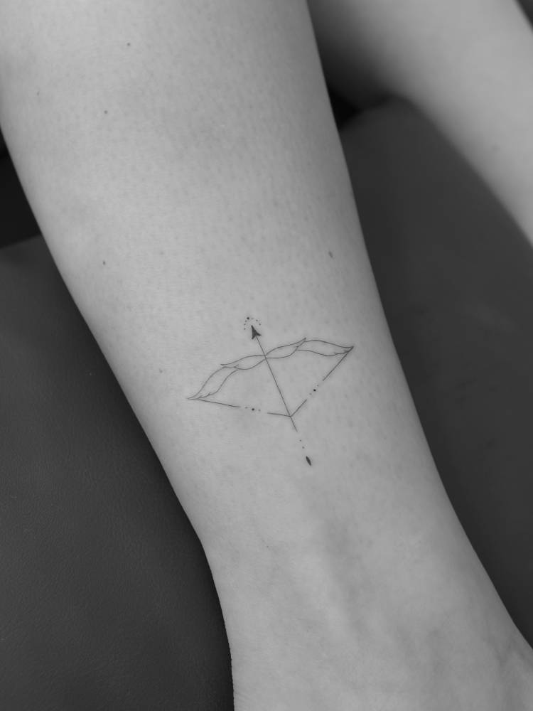 Bow and arrow in fine line style tattooed on the ankle.