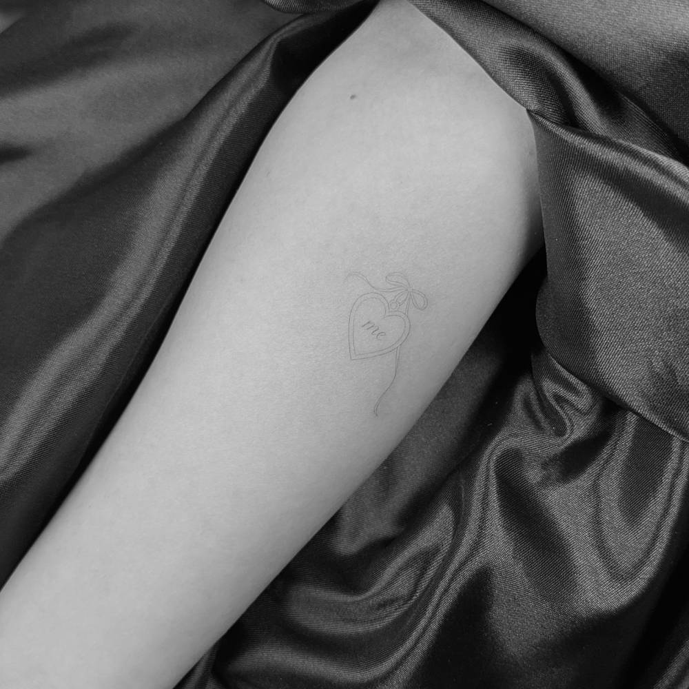 Heart pendant with the word "me" tattooed on the inner forearm.