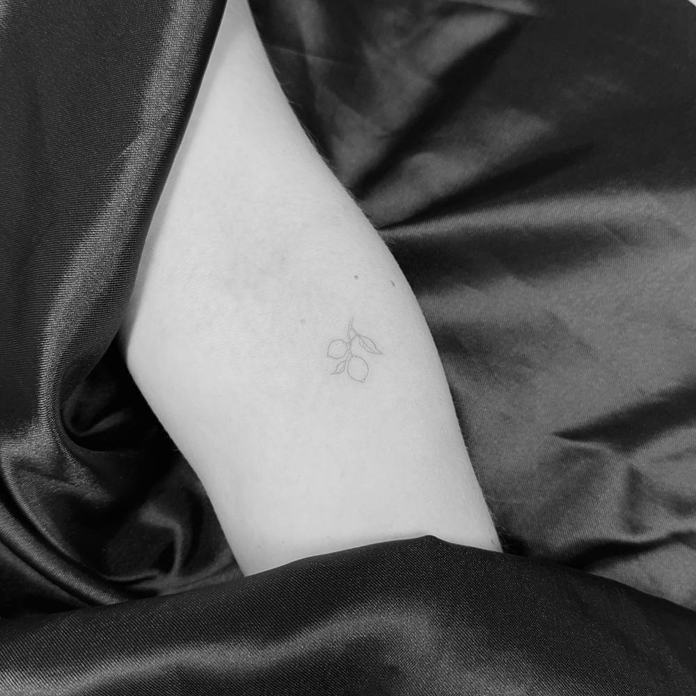 Tiny minimalistic lemons tattooed on the inner forearm, fine line style.
