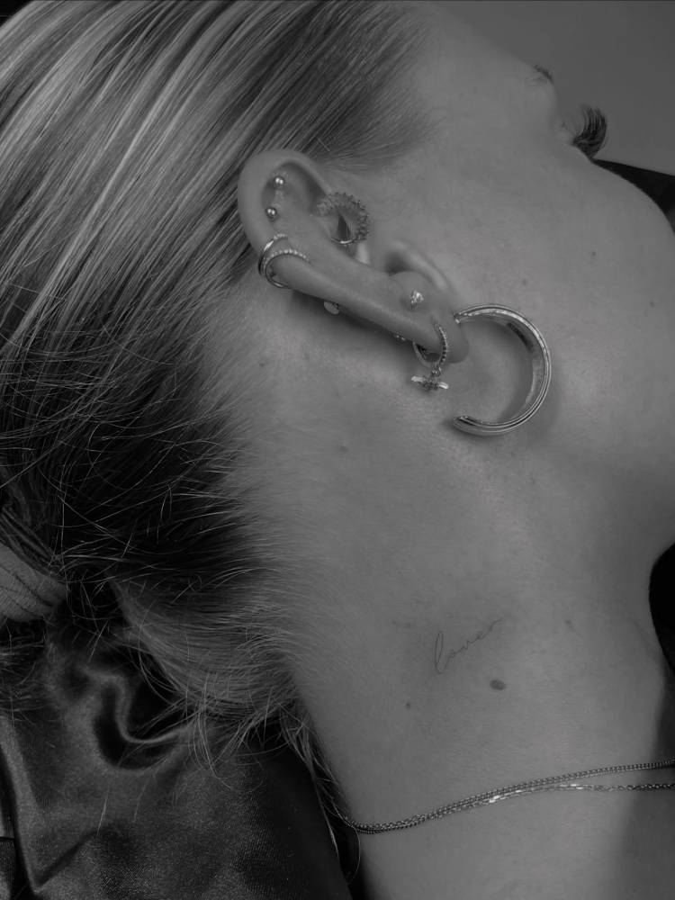 Handwritten word "lover" tattoo located on the neck.