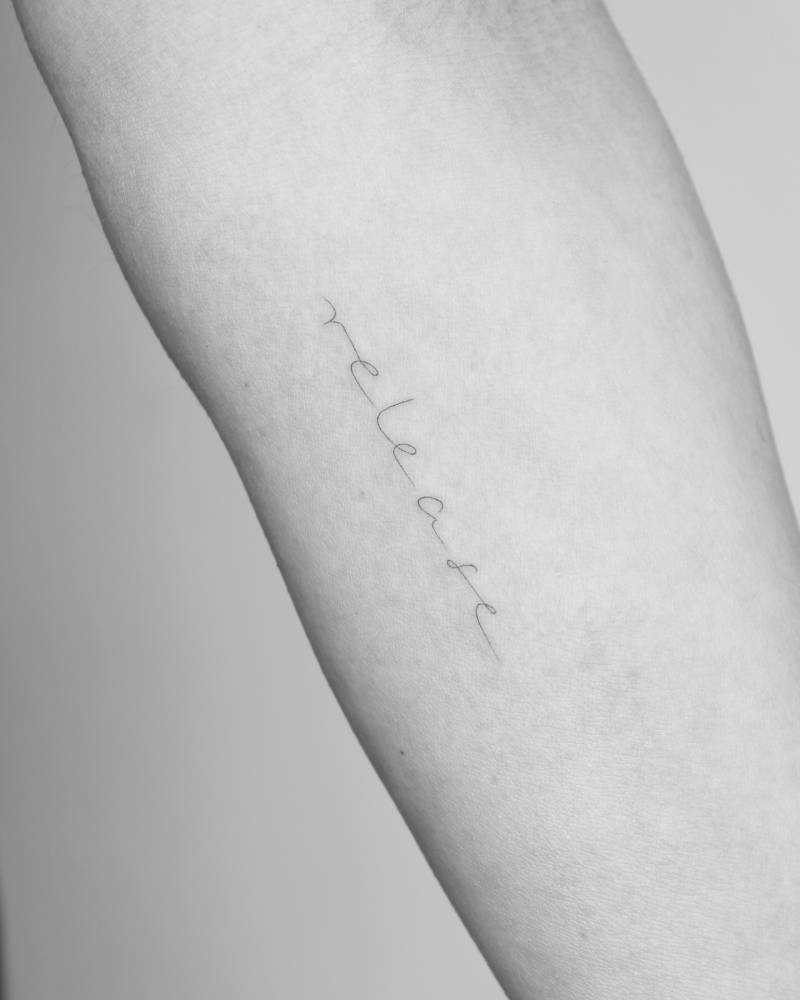 "Release" lettering tattoo handwritten on the inner forearm.