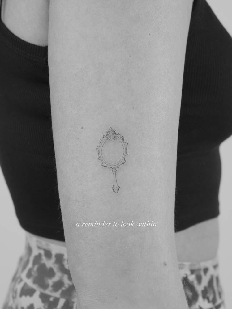 Hand mirror tattoo located on the upper arm, done in fine line style.