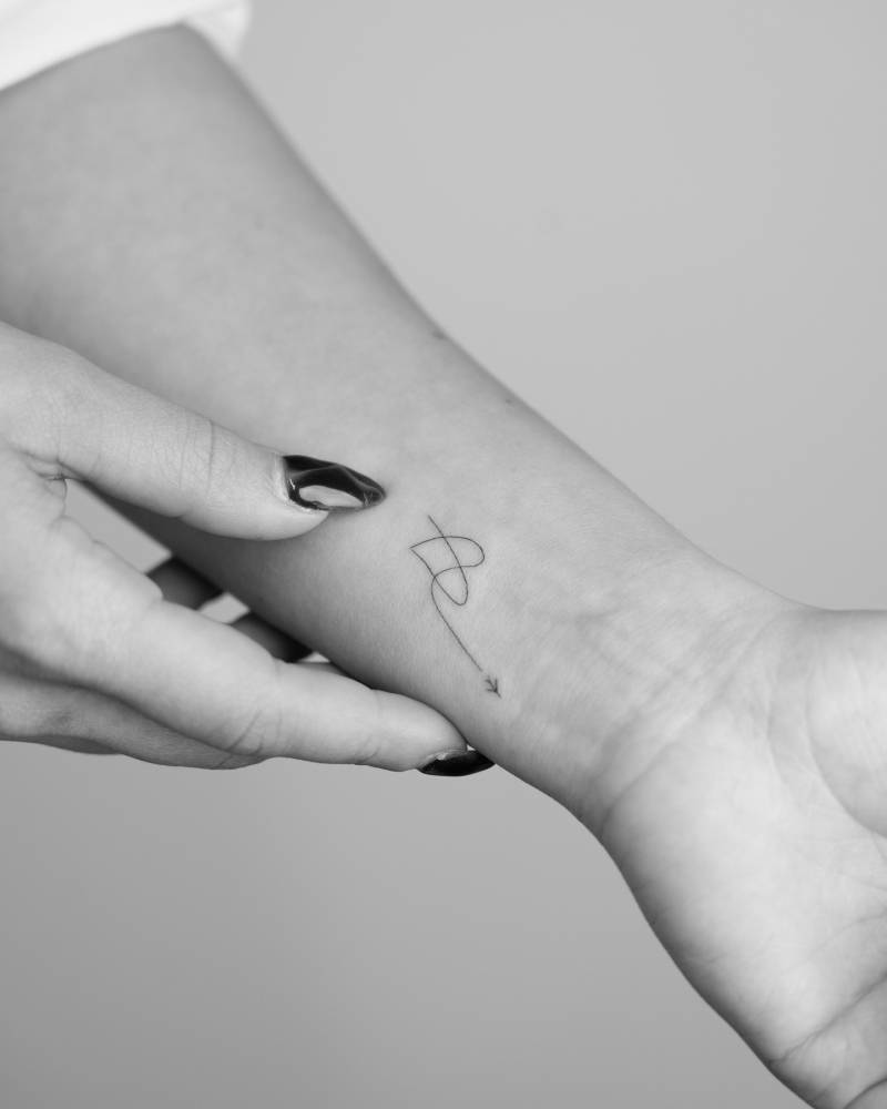 Minimalistic style airplane and heart tattoo located on the wrist.