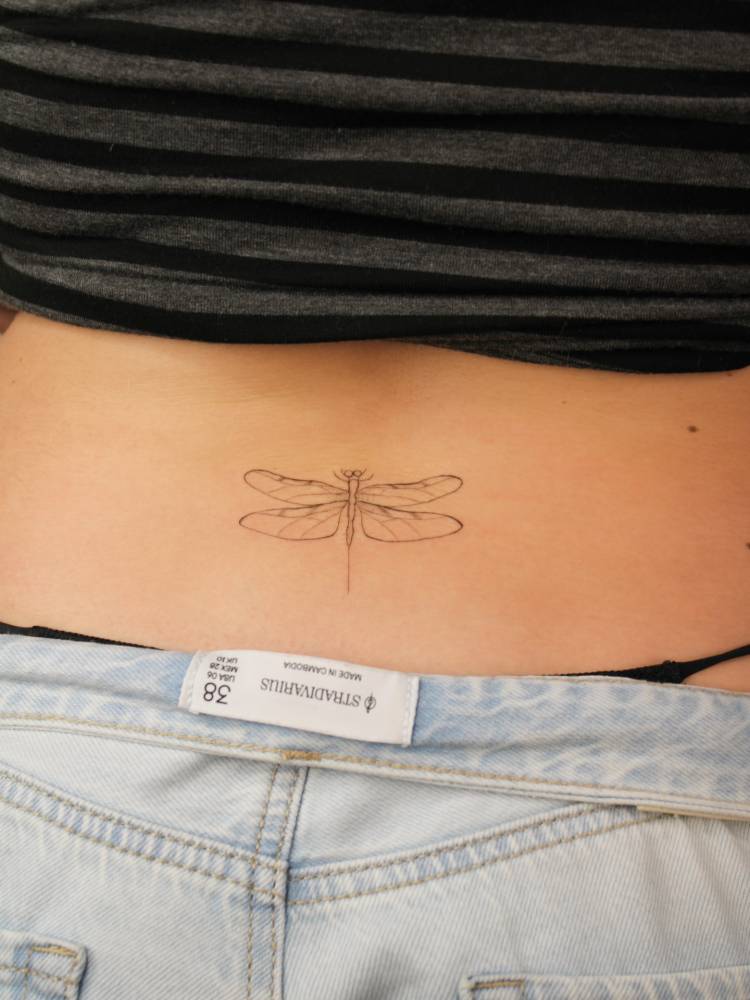 Tattoo of a dragonfly in fine line style located on the lower back.