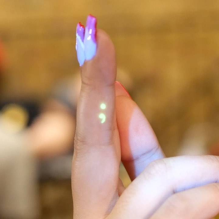 UV ink semicolon tattoo located on the finger.