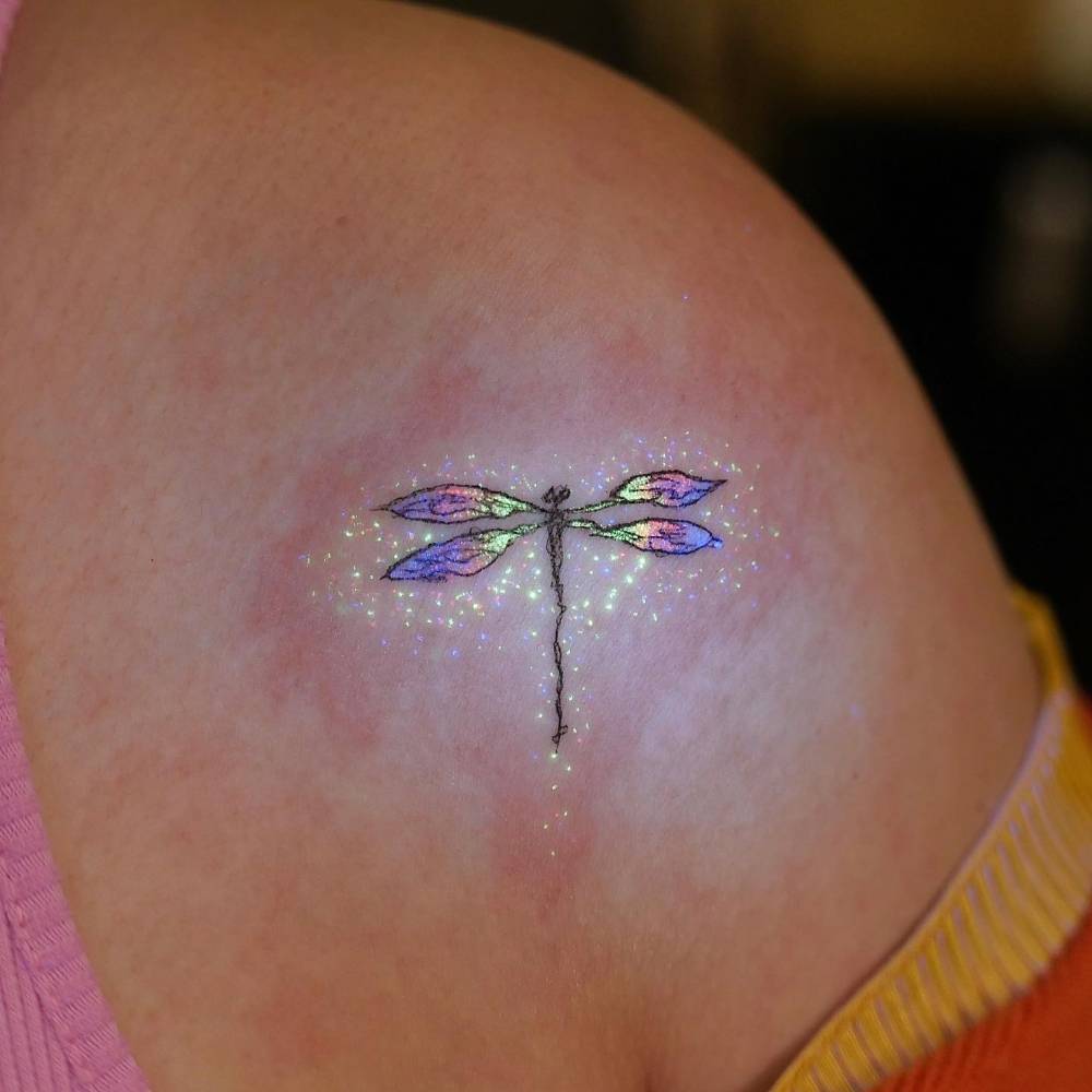 Illustrative style UV ink dragonfly tattoo placed on the shoulder.